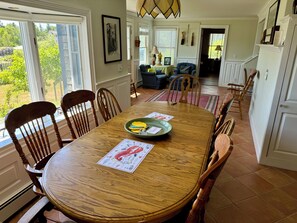 A dining area with a wooden table, chairs, and a view of the outdoors. - Comfy "Mini-estate" on Iconic Corea Harbor (Gouldsboro)