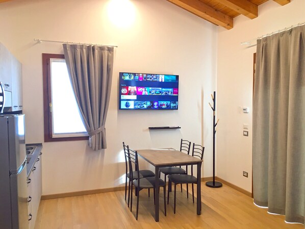 A dining area with a table and chairs, a television mounted on the wall displaying various channels, and a window with curtains. - Ca' Rosin Meolo - Camera relax e privacy (Meolo)