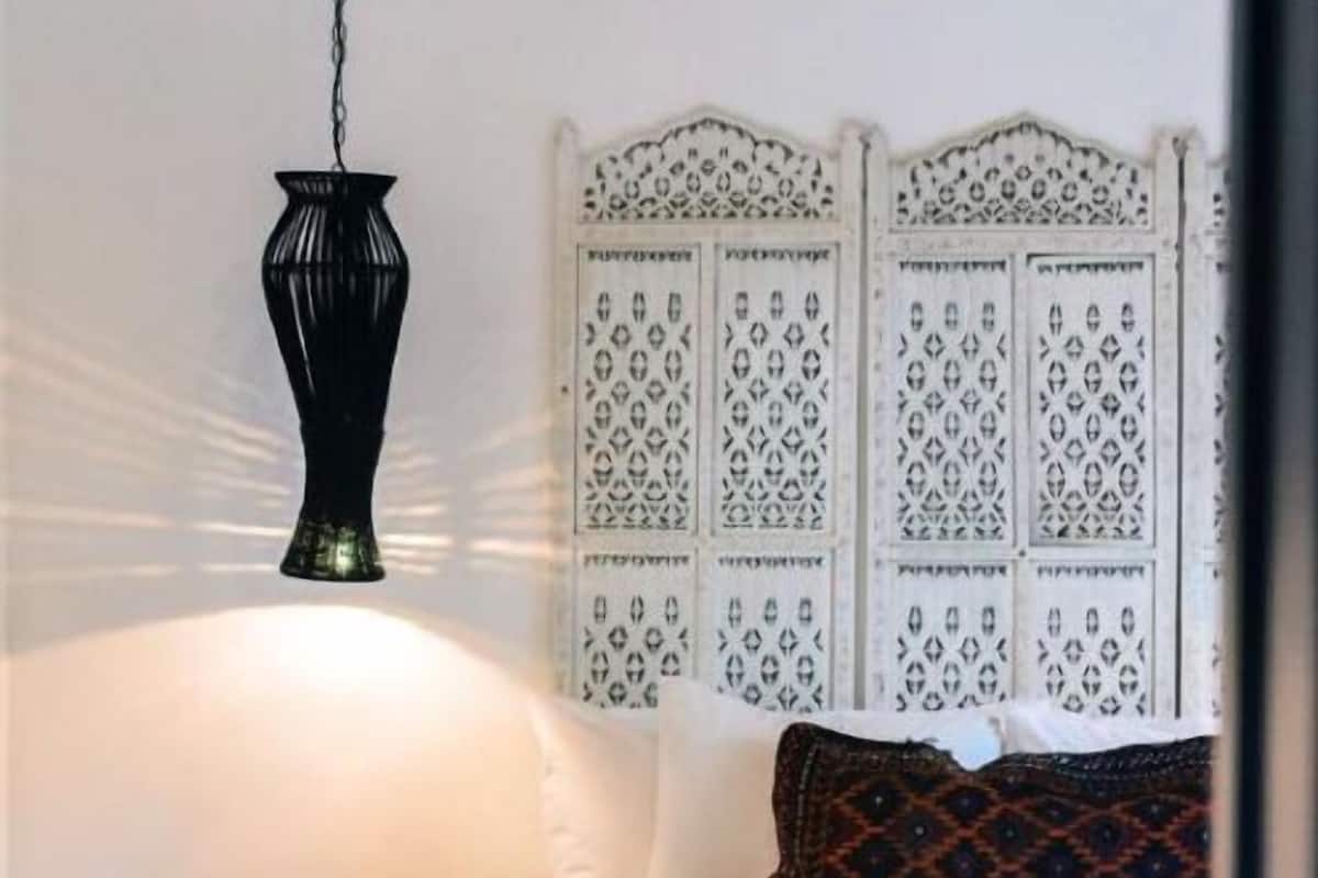 A bedroom with a bed, a hanging lamp, a patterned headboard, and a small bedside table.