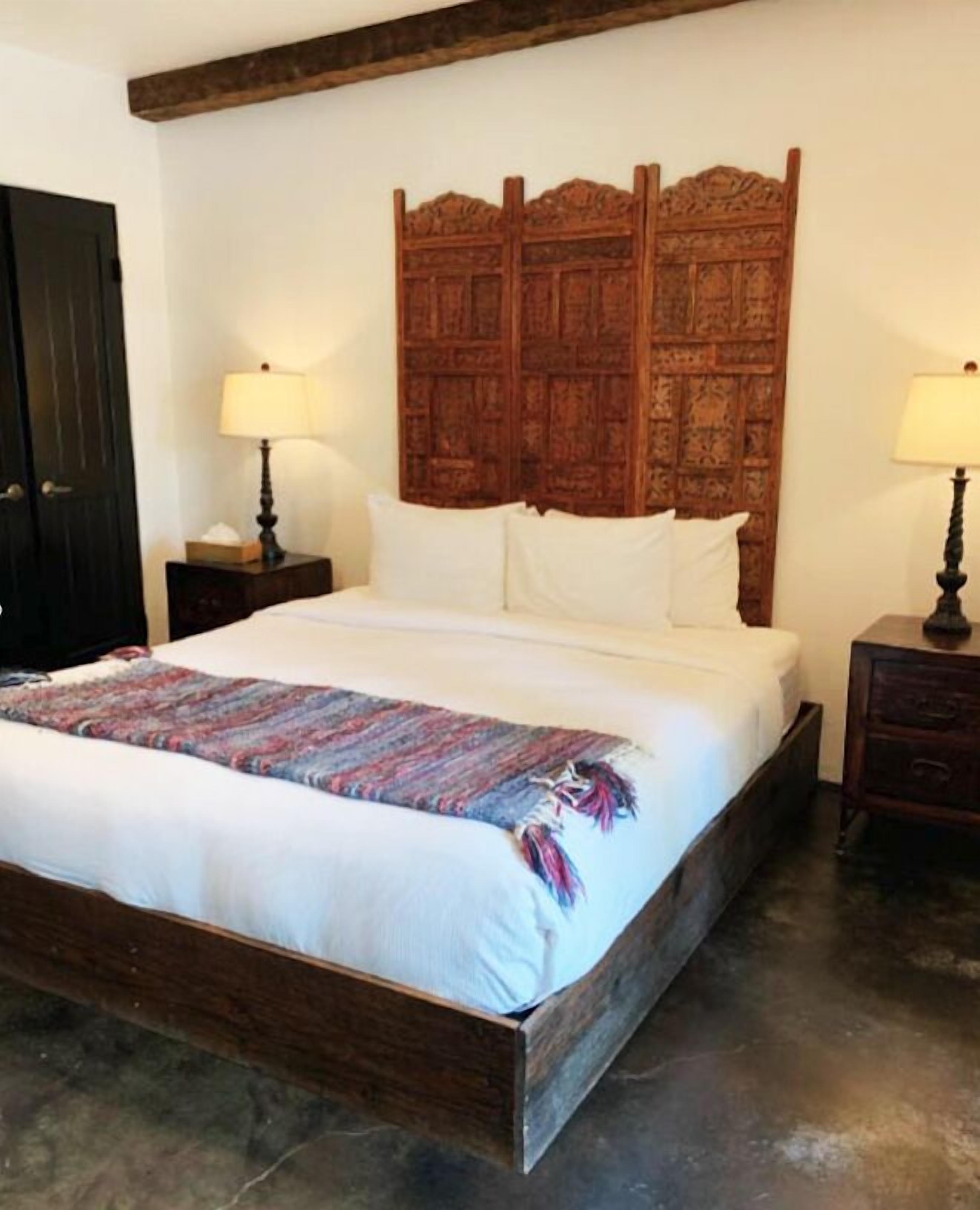 A bedroom with a wooden headboard, a large bed with white linens, two bedside tables with lamps, and a dark wooden wardrobe.