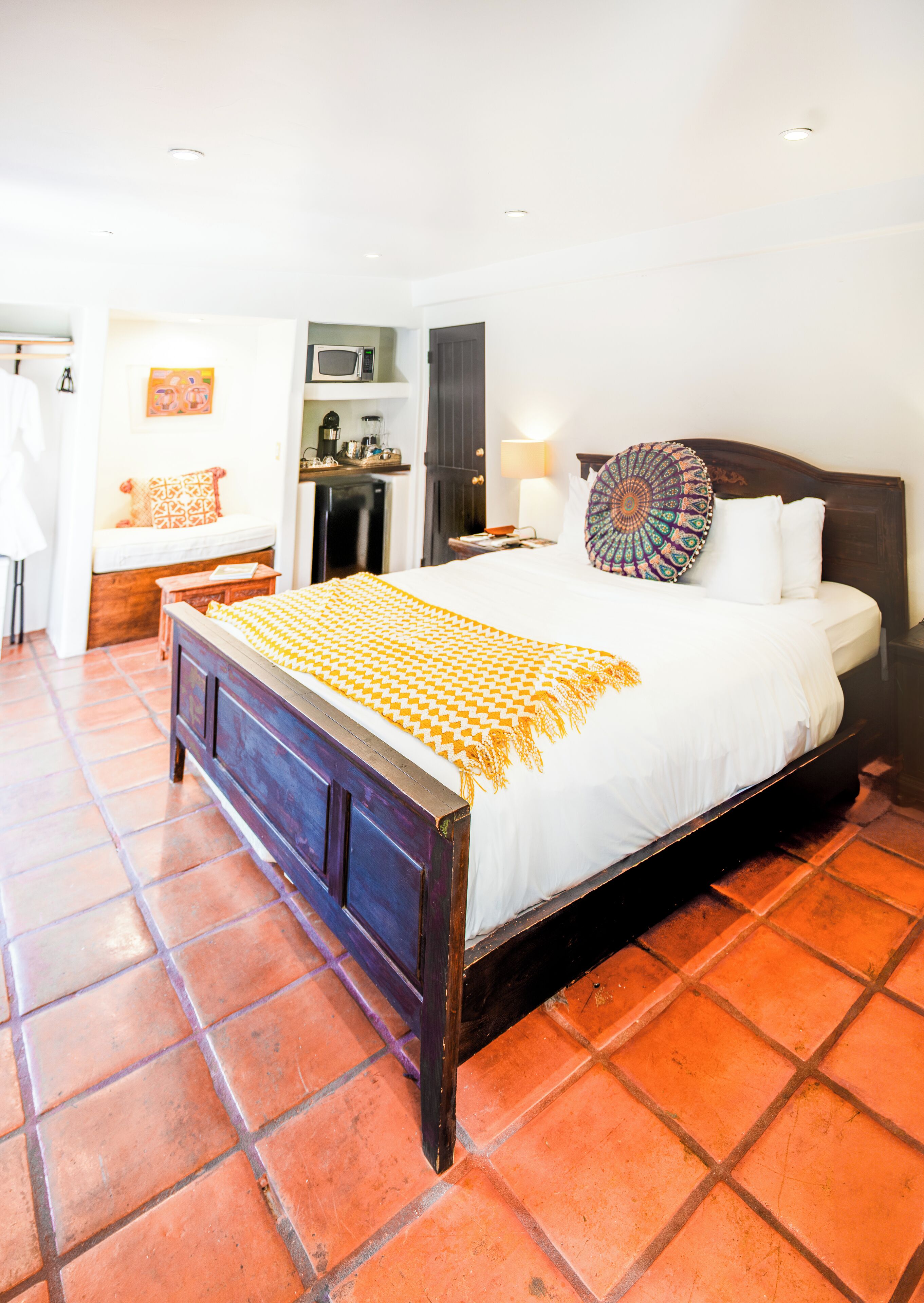 A bedroom with a wooden bed, a white mattress, a patterned throw, and a tiled floor.