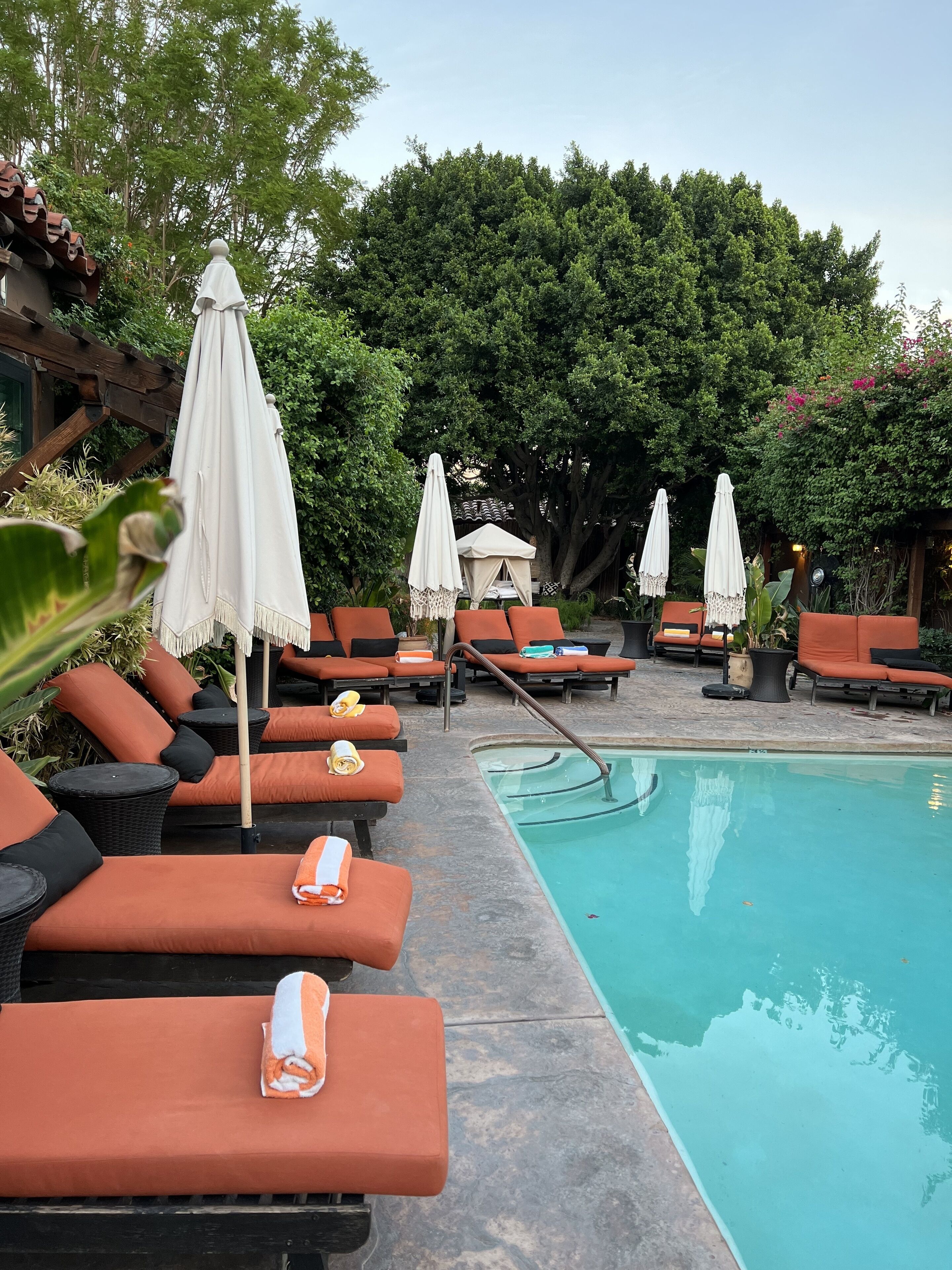 A poolside area with orange lounge chairs, white umbrellas, and a clear blue pool.