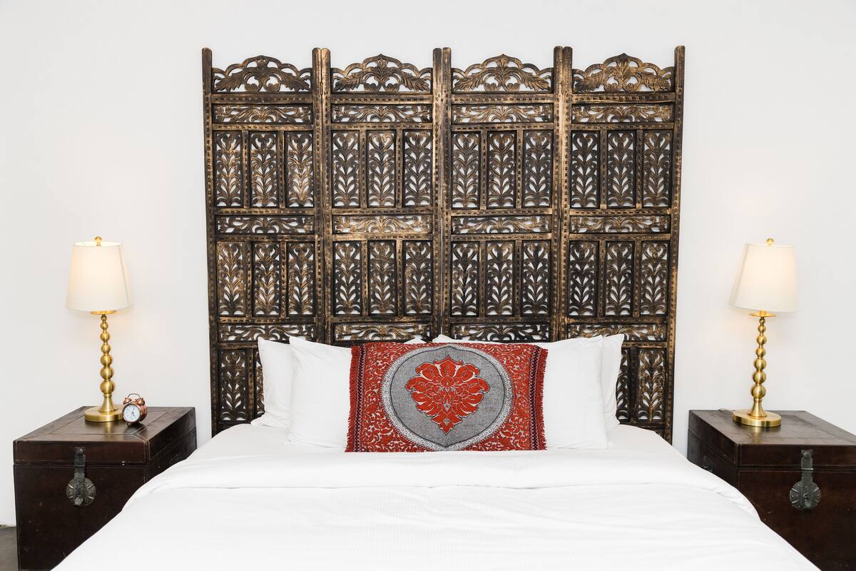 A bed with a decorative headboard, two bedside tables with lamps, and a clock on one of the tables.
