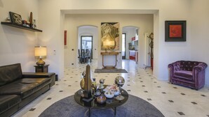A spacious living room with a black leather sofa, a round coffee table with decorative items, a purple armchair, and a large abstract painting on the wall.