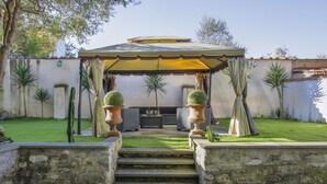 A covered outdoor seating area with steps leading up to it, surrounded by cacti and a white wall.