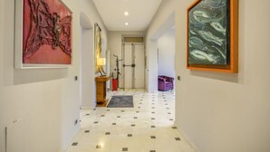 A hallway with artwork on the walls, a door at the end, and a purple chair in the corner.