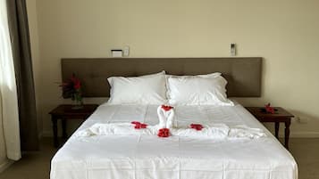 Una cama grande con sábanas blancas y flores rojas dispuestas sobre el cubrecolchón. Hay dos mesitas de noche con lámparas y un ventilador de techo.