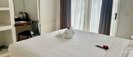 A hotel room with a neatly made bed, a desk with a chair, and a window with curtains.