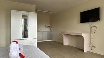 A hotel room with a bed, a desk, a TV, and a kitchenette.