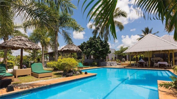 A swimming pool with lounge chairs and thatched umbrellas, surrounded by palm trees and a clear sky. - Coconut Palms Resort & Diamond Casino (Port Vila)