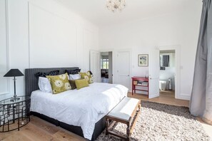 Un dormitorio con cama, mesita de noche, lámpara y vista al baño.