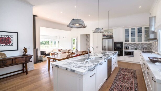 Cocina moderna con armarios blancos, una isla de mármol, iluminación colgante y vistas al área de comedor.