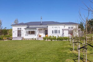 Ein zweistöckiges Haus mit überdachter Veranda, Schornstein und gepflegtem Rasen.