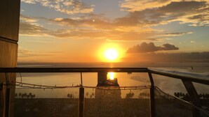 A sunset view from a balcony with a railing, overlooking a body of water and a distant shoreline.