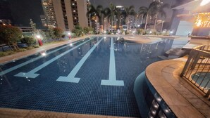 A swimming pool with clear lane markings, surrounded by palm trees and modern buildings.