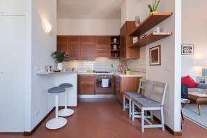 Une cuisine de taille réduite, avec des meubles de rangement en bois, une cuisinière à gaz et deux tabourets de bar.