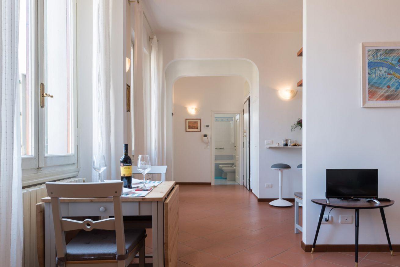 A room with a dining table, chairs, a television, and a view of a bathroom.