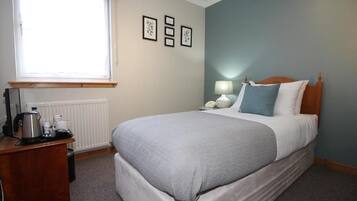 Una habitación de hotel con cama, mesita de noche, lámpara y ventana con persianas.