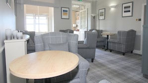 A modern hotel room with grey upholstered seating, a round wooden table, and framed artwork on the walls. - Temple View Hotel (Isle of North Uist)