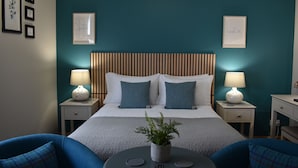 A neatly arranged hotel room with a bed, two bedside tables with lamps, a small round table with a plant, and two blue armchairs. - Temple View Hotel (Isle of North Uist)