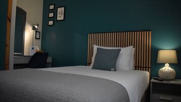 A neatly made bed with a grey blanket, a bedside lamp, and a nightstand with a remote control.