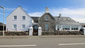 A white building with a stone facade, a stone wall, and a sign indicating a restaurant. - Temple View Hotel (Isle of North Uist)