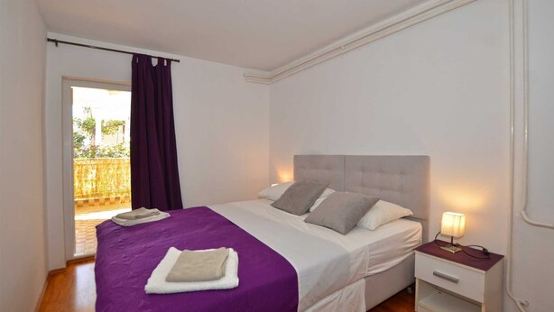 Un dormitorio con cama, mesita de noche, ventana con cortinas y vistas al exterior.