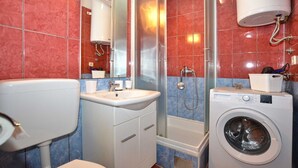Un baño con inodoro, lavabo, espejo, ducha y lavadora.