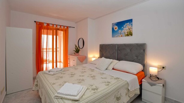 Une chambre à coucher comprenant un lit, des tables de chevet, une commode, une fenêtre avec des rideaux orange et un tableau accroché au mur.