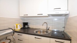 A compact kitchen with white cabinets, a stainless steel sink, a coffee maker, and a built-in induction cooktop.
