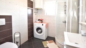 A compact bathroom with a washing machine, toilet, and shower.