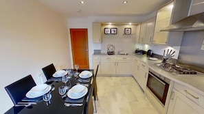 A modern kitchen with a dining area set for four. - Orange Apartments - 150e Rusbislaw Mansions (Aberdeen)