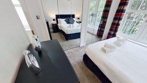 A hotel room with a bed, a desk, a mirror, and a view of the outdoors. - Orange Apartments - 150e Rusbislaw Mansions (Aberdeen)