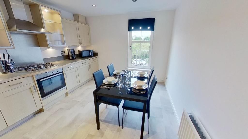 A modern kitchen with a dining table set for four, a built-in oven, and a window with curtains.