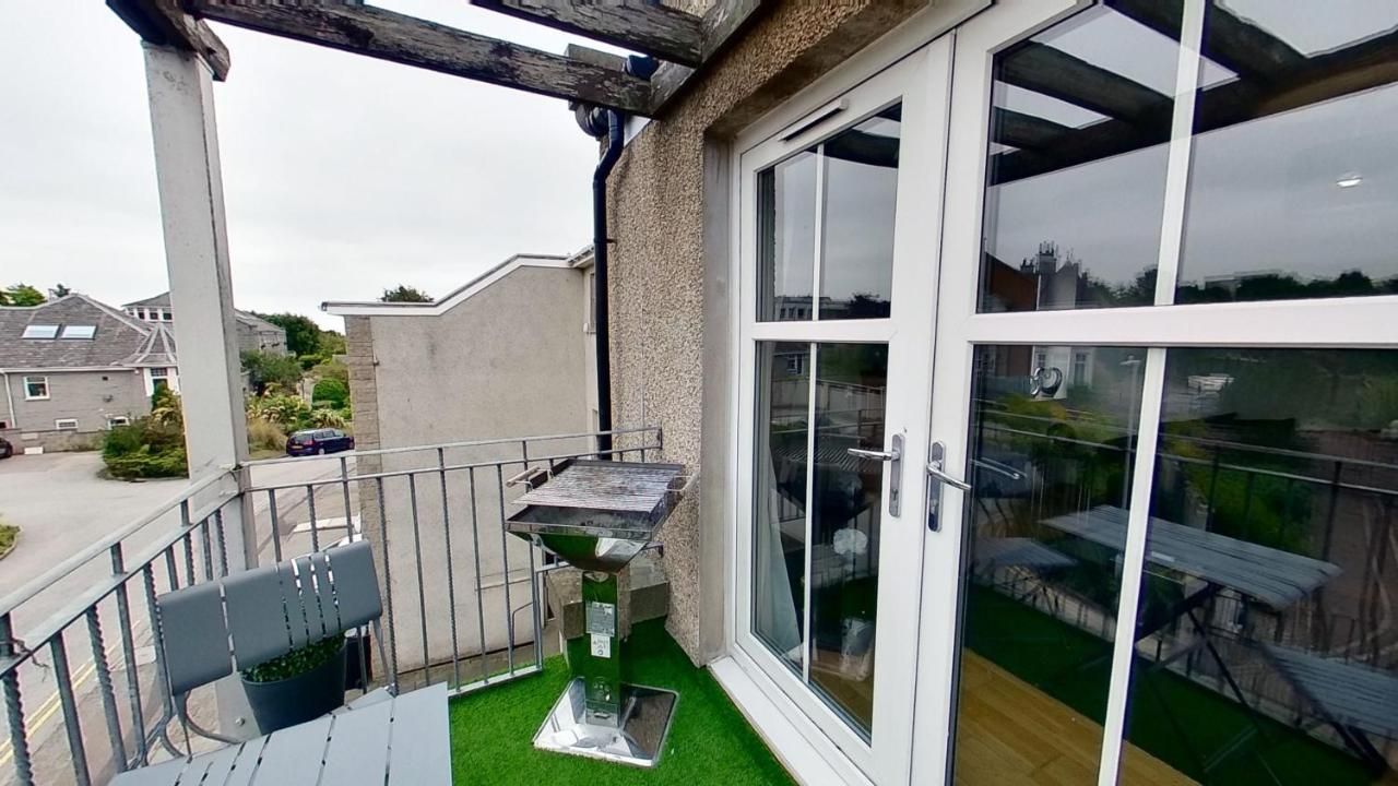 A balcony with a grill, a chair, and a table.