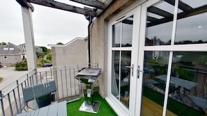 A balcony with a grill, a chair, and a table. - Orange Apartments - 150e Rusbislaw Mansions (Aberdeen)