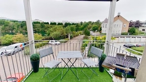 A balcony with a table and chairs, a grill, and a view of a residential area with trees and parked cars. - Orange Apartments - 150e Rusbislaw Mansions (Aberdeen)