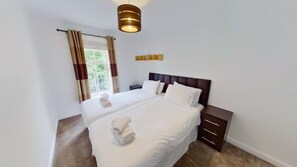 A hotel room with a large bed, a bedside table, a lamp, and a window with curtains. - Orange Apartments - 150e Rusbislaw Mansions (Aberdeen)