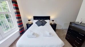 Una cama bien hecha con almohadas, dos lámparas de noche, un aparador y una ventana con cortinas.