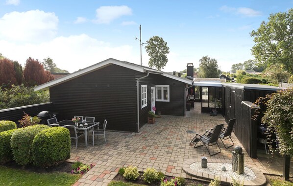 Una casa de madera oscura con un patio, un pequeño jardín y una barbacoa.