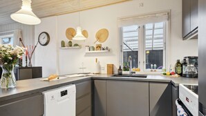Una cucina moderna con lavastoviglie, lavello e fornello. Sul piano di lavoro ci sono elementi decorativi e una finestra sopra il lavello.