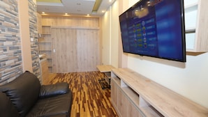 Una sala de estar moderna con piso de madera, un sofá de cuero, un televisor montado en la pared y un mueble de madera.