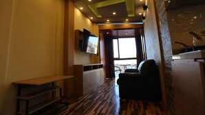 Un moderno vestíbulo de hotel con un banco de madera, un televisor de pantalla plana montado en la pared y un amplio ventanal que proporciona luz natural.