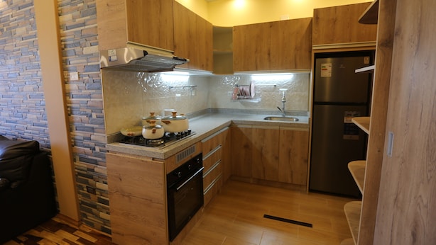 Una cocina compacta con armarios de madera, horno empotrado, refrigerador de acero inoxidable y salpicadero de piedra.