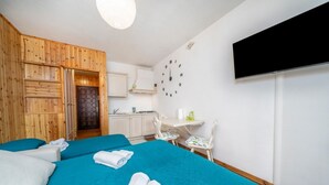A room with two beds, a wooden wardrobe, a kitchen area, a wall clock, and a flat-screen TV. - GuestHost - Da Crispe Studio - 550 m far from the Golf Club (Tarvisio)