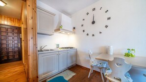 A kitchen with white cabinets, a clock on the wall, and a wooden door. - GuestHost - Da Crispe Studio - 550 m far from the Golf Club (Tarvisio)