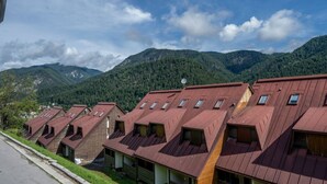 A row of chalet-style buildings with pitched roofs and dormer windows, set against a backdrop of forested mountains. - GuestHost - Da Crispe Studio - 550 m far from the Golf Club (Tarvisio)