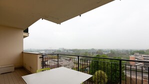 A balcony with a white table and green chairs, overlooking a cityscape with buildings and greenery. - GuestHost - Milan-Rubattino Comfy APT - with 2 Terrace (Milano)
