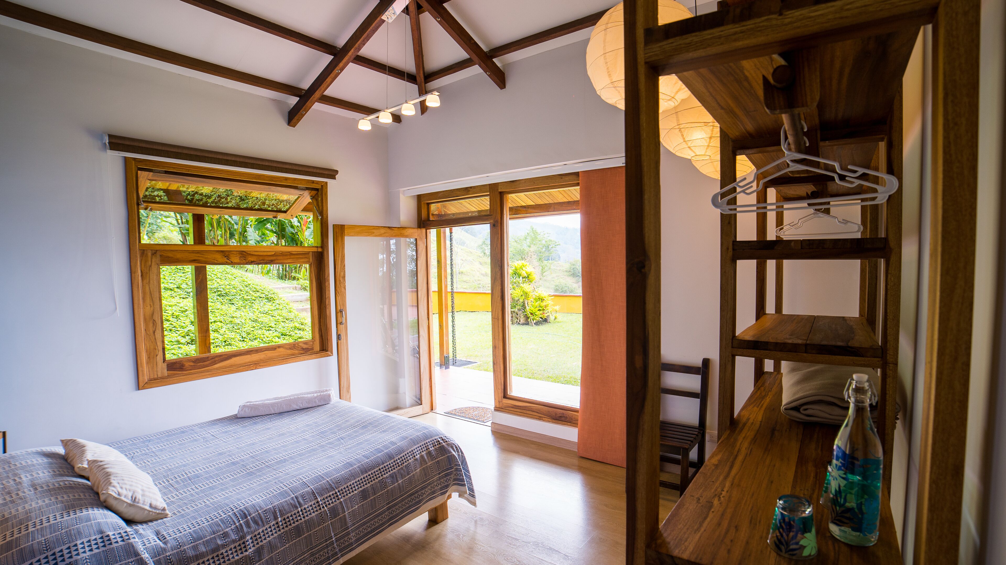 Ein Schlafzimmer mit einem Bett, einem Holzregal und Blick auf einen Garten durch ein Fenster.