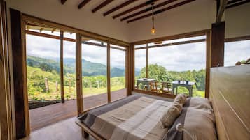Un dormitorio con una cama grande, vigas de madera y vistas a un paisaje exuberante.